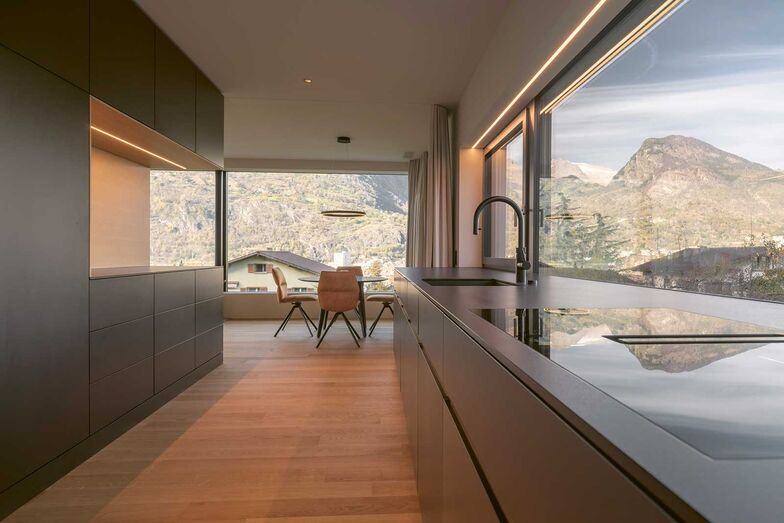 Die Familie kann den Ausblick sowohl beim Kochen als auch beim gemeinsamen Essen geniessen. Dazu fällt durch die grossen Fenster viel natürliches Tageslicht. Die Vorhänge sind nicht nur für die Glasfronten bestimmt, sondern auch für die flexible Raumaufteilung. Es handelt sich um schalldämpfende Akustikvorhänge.