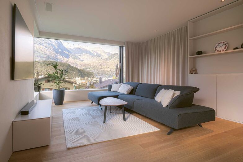 Der Vorhang hinter dem Sofa trennt den Wohnbereich von der Frühstücksecke. Die Schiene geht zwischen der Wand und dem Regal versteckt weiter und der Vorhang verschwindet bei Nichtgebrauch aus dem Sichtfeld. Diese clevere Lösung sorgt dafür, dass dem minimalistischen Stil kein Abbruch getan wird.