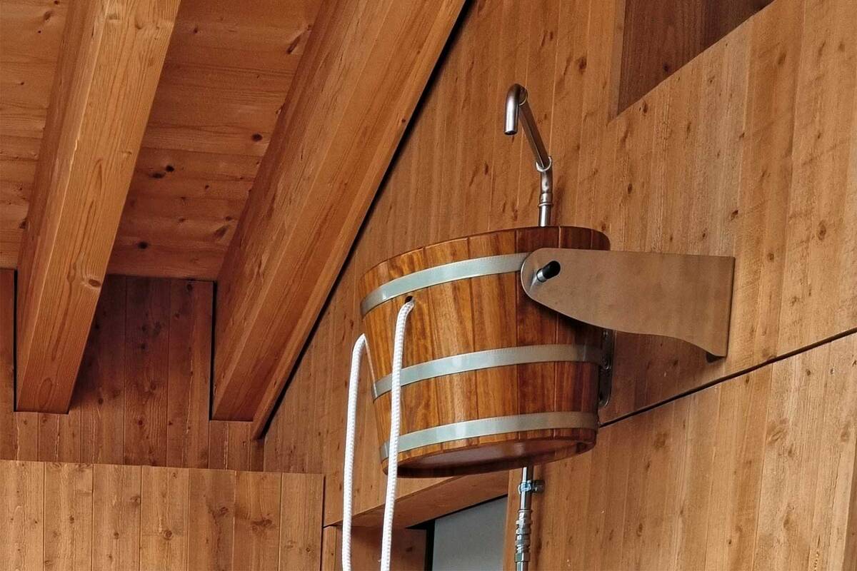 Die «Eimer-Schwalldusche» sorgt nach der Sauna für einen intensiven Kältereiz. Das Wasser, das oben eingefüllt wird, kann per Zug am weissen Seil entleert werden. Angelehnt am rustikalen Design, bietet Fitness-Partner eine moderne Variante des Klassikers. Fitness-Partner AG.