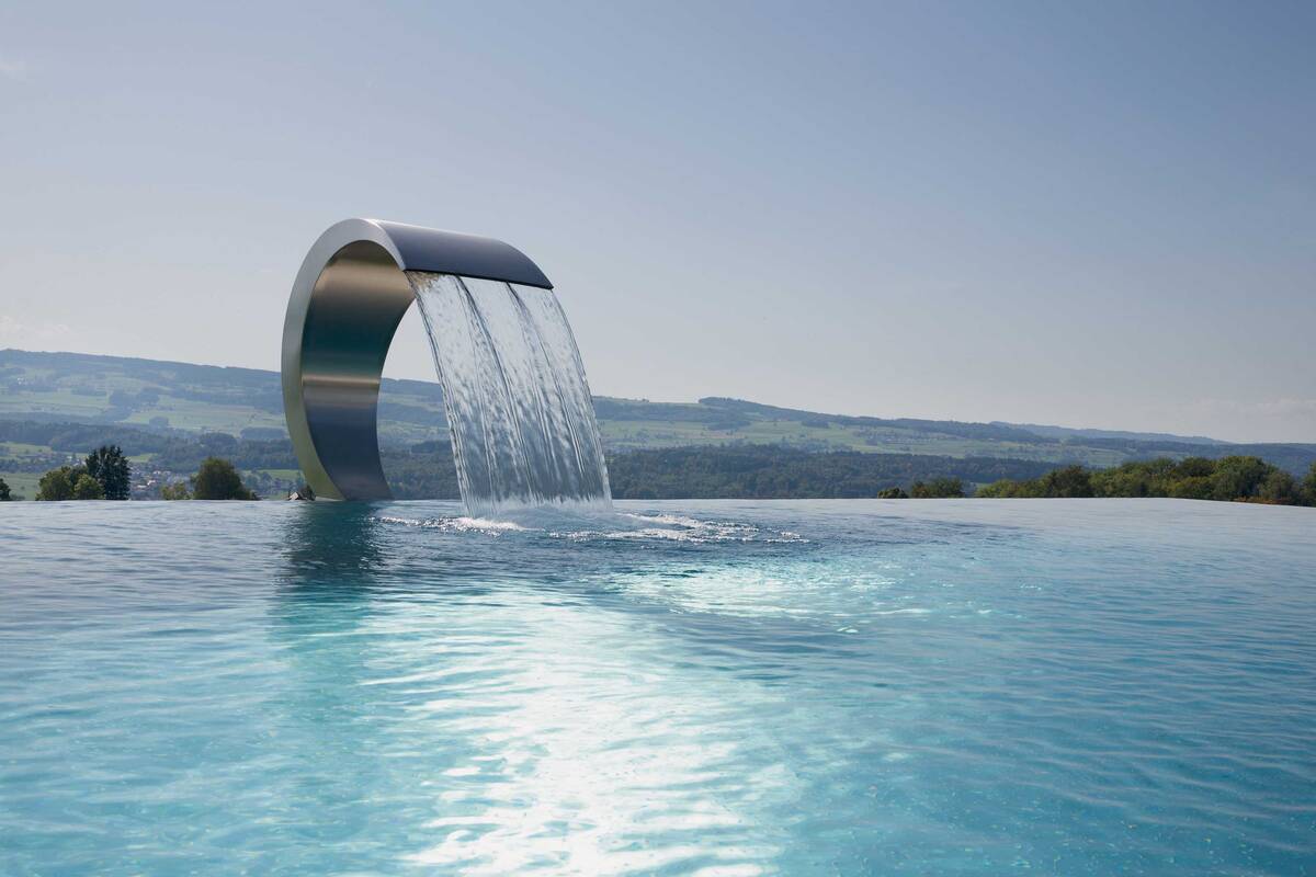 Einfach erfrischend: Eine Schwallbrause ist Blickfang, Massagestation und Frischekick in einem. Diese krönt einen Infinity-Pool aus Edelstahl. Die aussergewöhnliche Anlage mit fast 50 Quadratmetern Wasserfläche wurde von der Vereinigung «Aqua Suisse» zum schönsten privaten Freibad der Schweiz gekürt. Vita Bad AG.