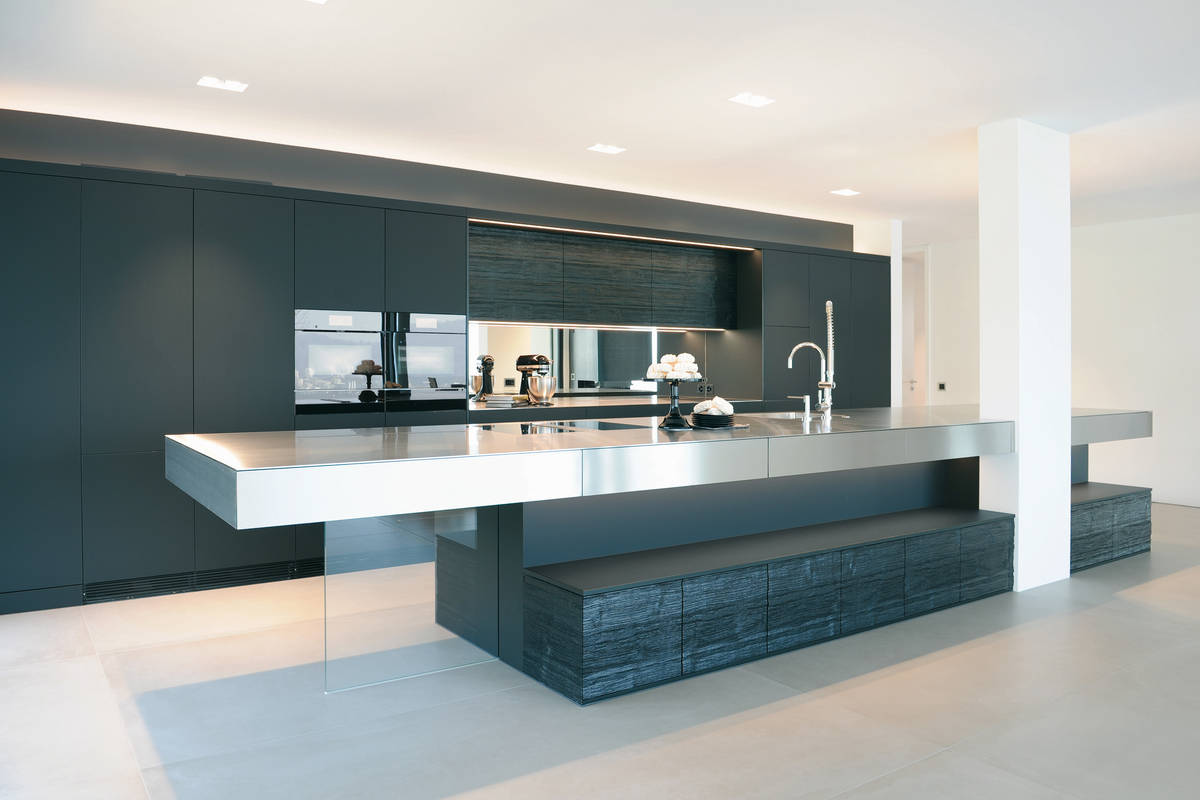 Mattschwarze Fronten, Strukturholz, Profiarmatur, Spiegelrückwand und eine langgezogene Arbeitsplatte aus Chromstahl: Diese edle Küche ist ein echter Hingucker. Brunner Küchen.