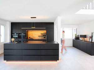 Durch das sägerohe Eichenfurnier, das schwarz gebeizt und lackiert wurde, werden Chalet-Charme und State-of-the-art kombiniert. Durch die Sockelbeleuchtung wirkt die Insel schwebend leicht. Elbau Küchen AG.