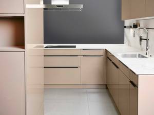 Elegant und zeitlos: Die Seitenwände  in weisser Marmoroptik ergeben  mit den crème-beigen Küchenschränken  und der schnörkellosen Armatur ein  harmonisches Gesamtbild.  Sabag Biel/Bienne AG.