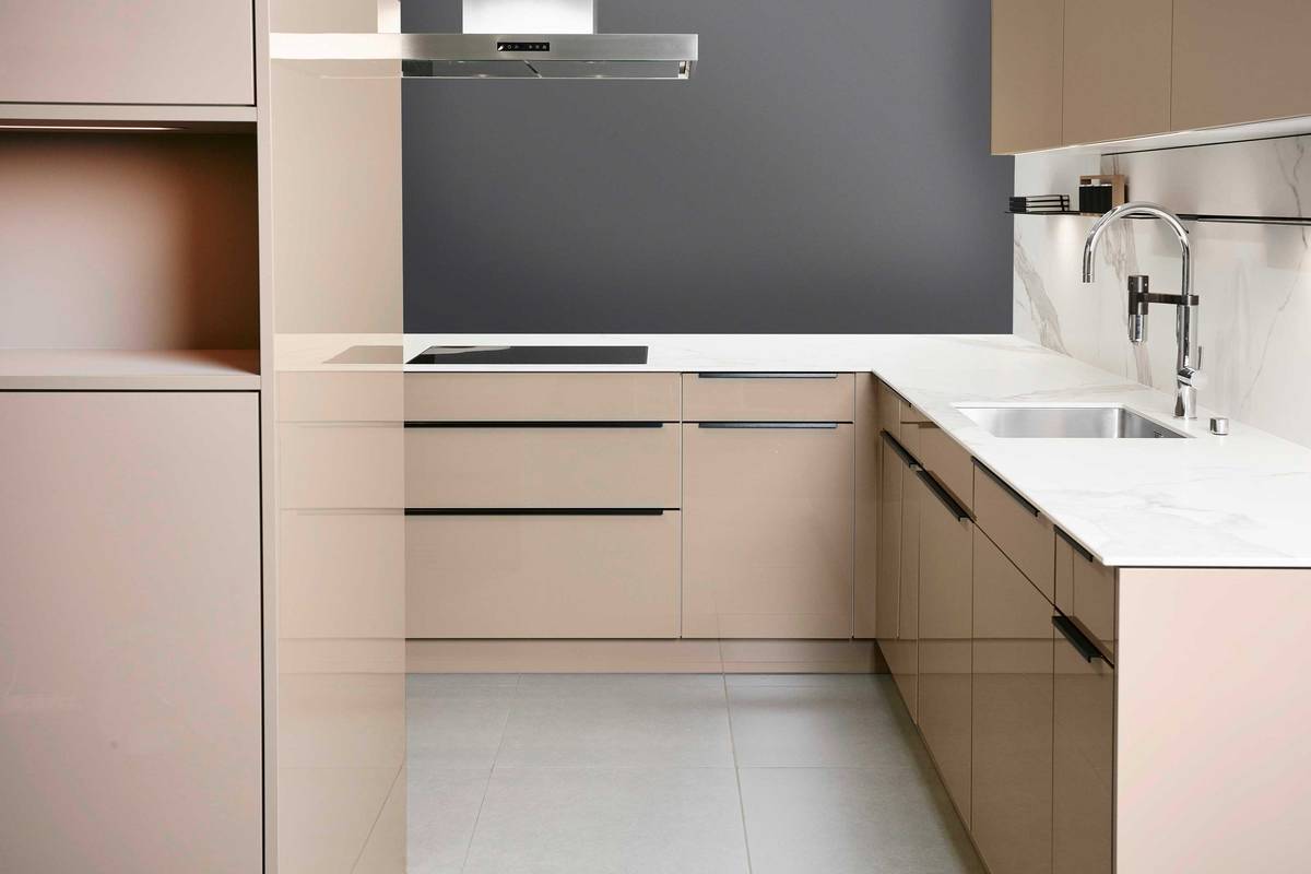 Elegant und zeitlos: Die Seitenwände  in weisser Marmoroptik ergeben  mit den crème-beigen Küchenschränken  und der schnörkellosen Armatur ein  harmonisches Gesamtbild.  Sabag Biel/Bienne AG.