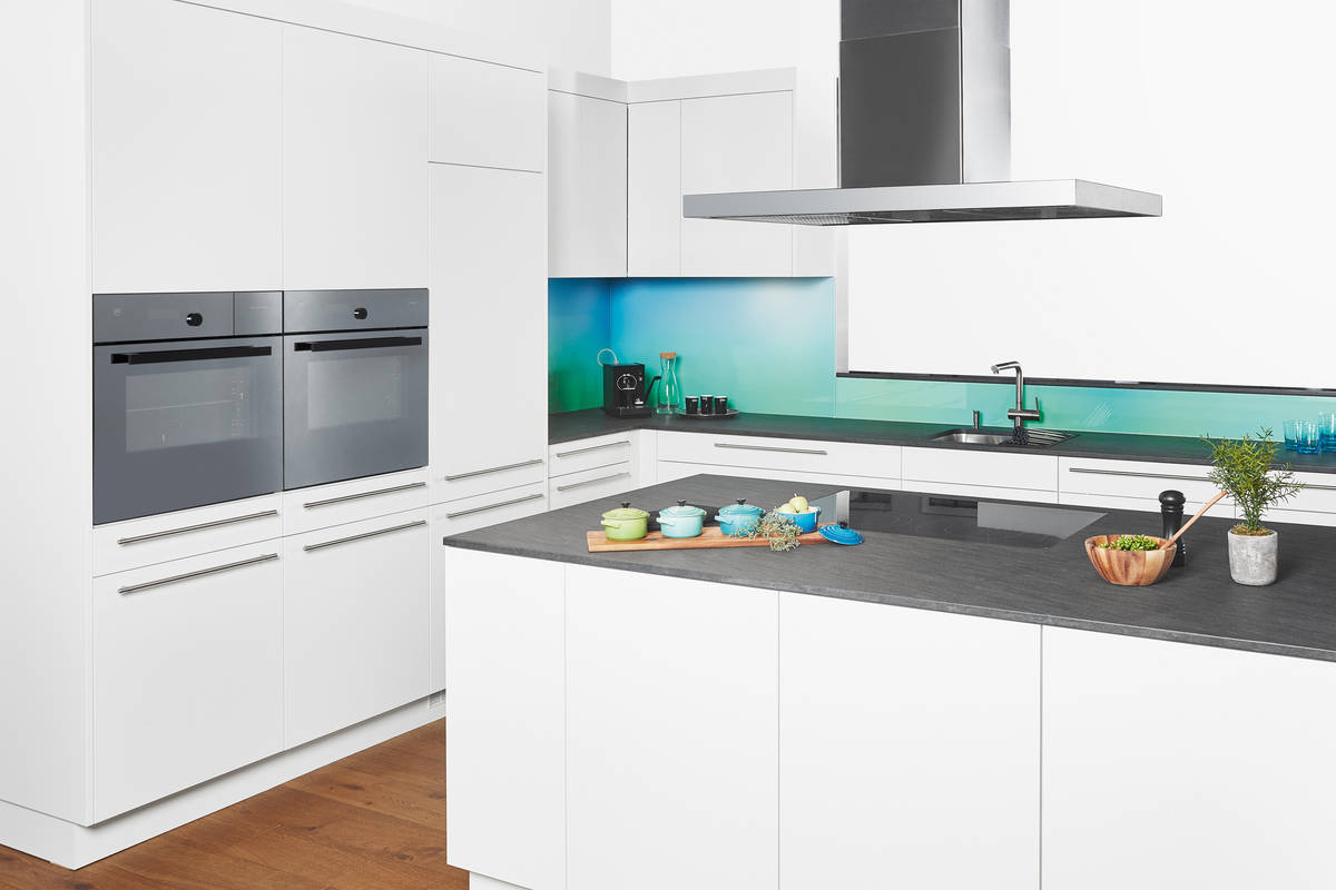 Der Hingucker: die grün-blaue Glasrückwand. In Kombination mit der zurückhaltenden Granitabdeckung und dem stilvollen Weiss wird keinem die Show gestohlen. Sabag.