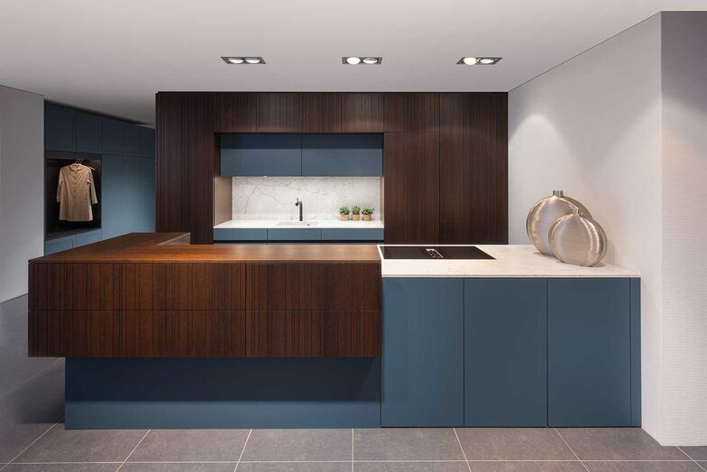 Ein Tupfer Farbe: Es muss nicht immer Schwarz und Weiss sein. Diese Showroom-Küche der Elbau Küchen AG besticht durch den geschickten Einsatz von Holz und Farbe sowie eine Ablage und ein Becken aus italienischem Naturstein. Die Küche kommt durch die raffinierte Farb-, Material- und Formkombination bei der Kücheninsel mit einer ausgeprägten Leichtigkeit daher. Die asymmetrische Rillenfront «Chilli» lässt Fugen unsichtbar wirken und betont den Charakter.   Elbau Küchen AG, www.elbau.ch