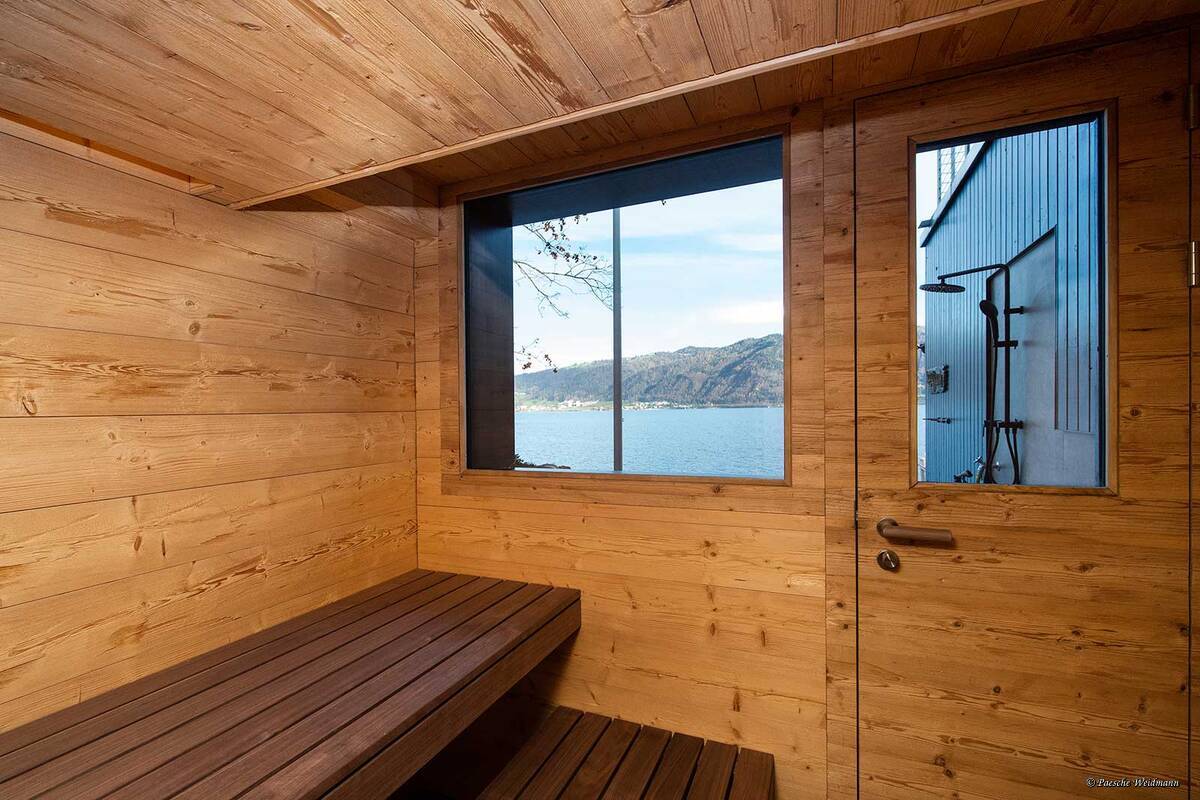 Saunieren mit schönem Ausblick auf den See: Diese Sauna liegt in einem Bootshaus. Das dunkle Altholz setzt ein Gegenspiel zur Natur draussen. Indirektes, farbiges Licht zaubert zusätzlich eine beruhigende Atmosphäre in den Raum. Küng Wellness AG.