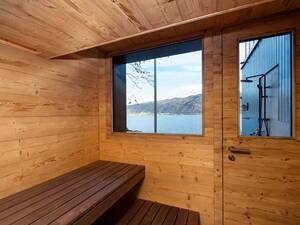 Saunieren mit schönem Ausblick auf den See: Diese Sauna liegt in einem Bootshaus. Das dunkle Altholz setzt ein Gegenspiel zur Natur draussen. Indirektes, farbiges Licht zaubert zusätzlich eine beruhigende Atmosphäre in den Raum. Küng Wellness AG.