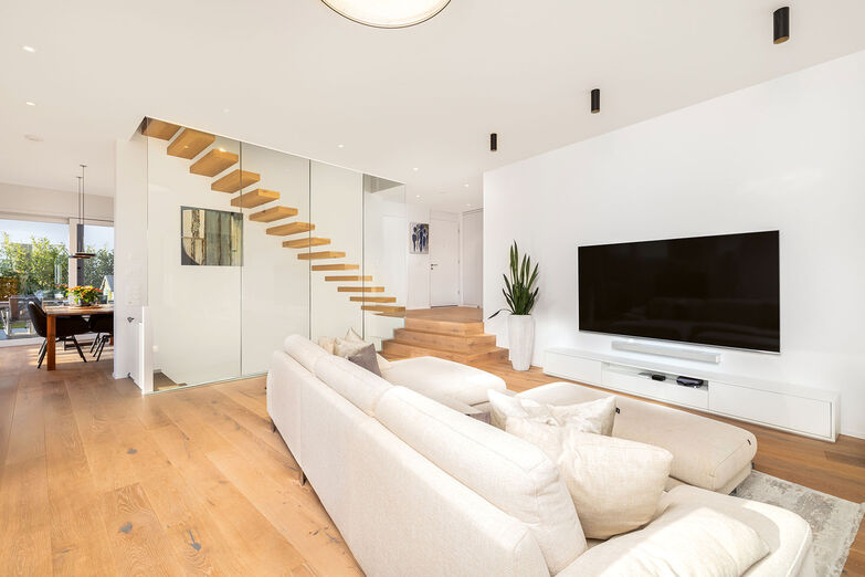 Eine elegante Treppe mit Glasgeländer verbindet den Eingangsbereich mit dem Wohnraum und sorgt für ein grosszügiges Raumgefühl.