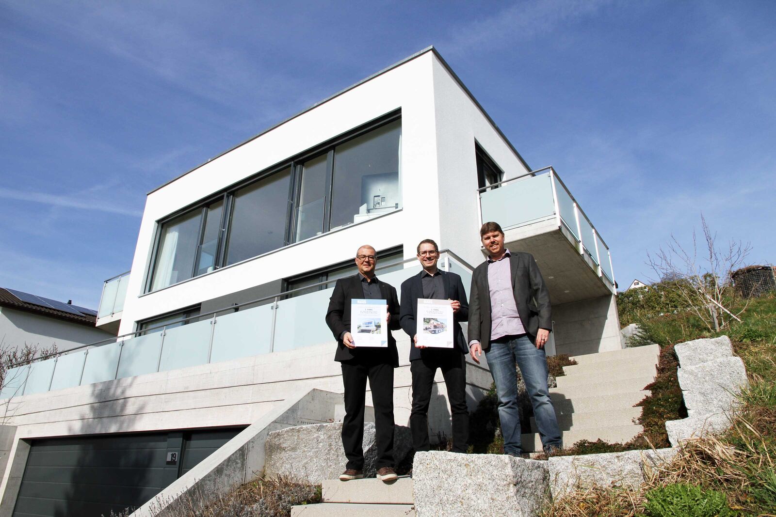 Zertikatsübergabe vor dem Massivhaus von Kobelt, das den 3. Platz bei der Publikumswahl erreichte. Von links: Bruno Locher, Leiter Architektur und Vertrieb, Reto Ebneter, Architekt, beide Kobelt AG, und Marcel Hablützel, Head of Sales & Marketing, Etzel Verlag.