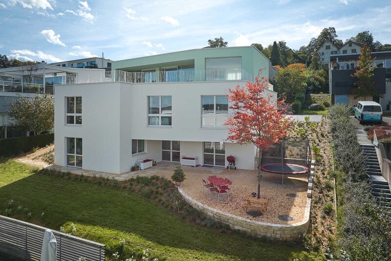 An der hangseitigen Fassade erweitern grosse, einladende Terrassen den Wohnraum ins Freie. Ob draussen oder drinnen – überall  ist das Farbkonzept erkennbar, das Mint- und helle Crème- und Beigetöne vortrefflich vereint.