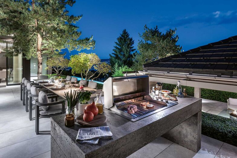 Der Essbereich wird durch zwei immergrüne Nadelgehölze strukturiert, dazwischen sind der grosse Esstisch und der Aussengrill platziert.