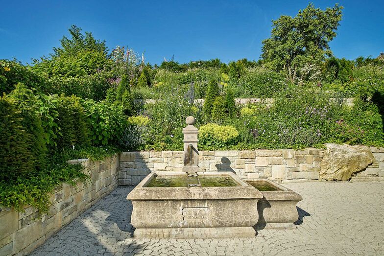 Ein antiker Brunnen inmitten eines romantischen Gartens mit üppigen Staudenpflanzen ist der optimale Platz für eine kleine Auszeit vom Alltag. Gartencenter Hoffmann AG, www.gartencenter-hoffmann.ch