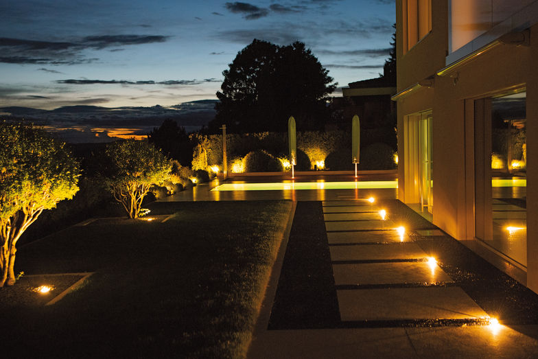 Eine dezente Beleuchtung weist den Weg über grossformatige Platten zum Poolbereich.