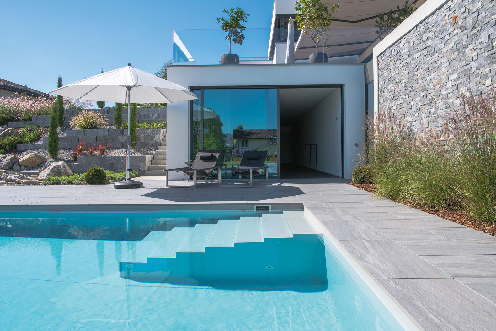 Skimmerbecken aus Beton mit Folienauskleidung, Rollladenabdeckung, automatischer Filtertechnik und Wasseraufbereitung. Beheizung über Wärmetauscher. Beleuchtung LED warmweiss. Zireg Ziswiler AG.