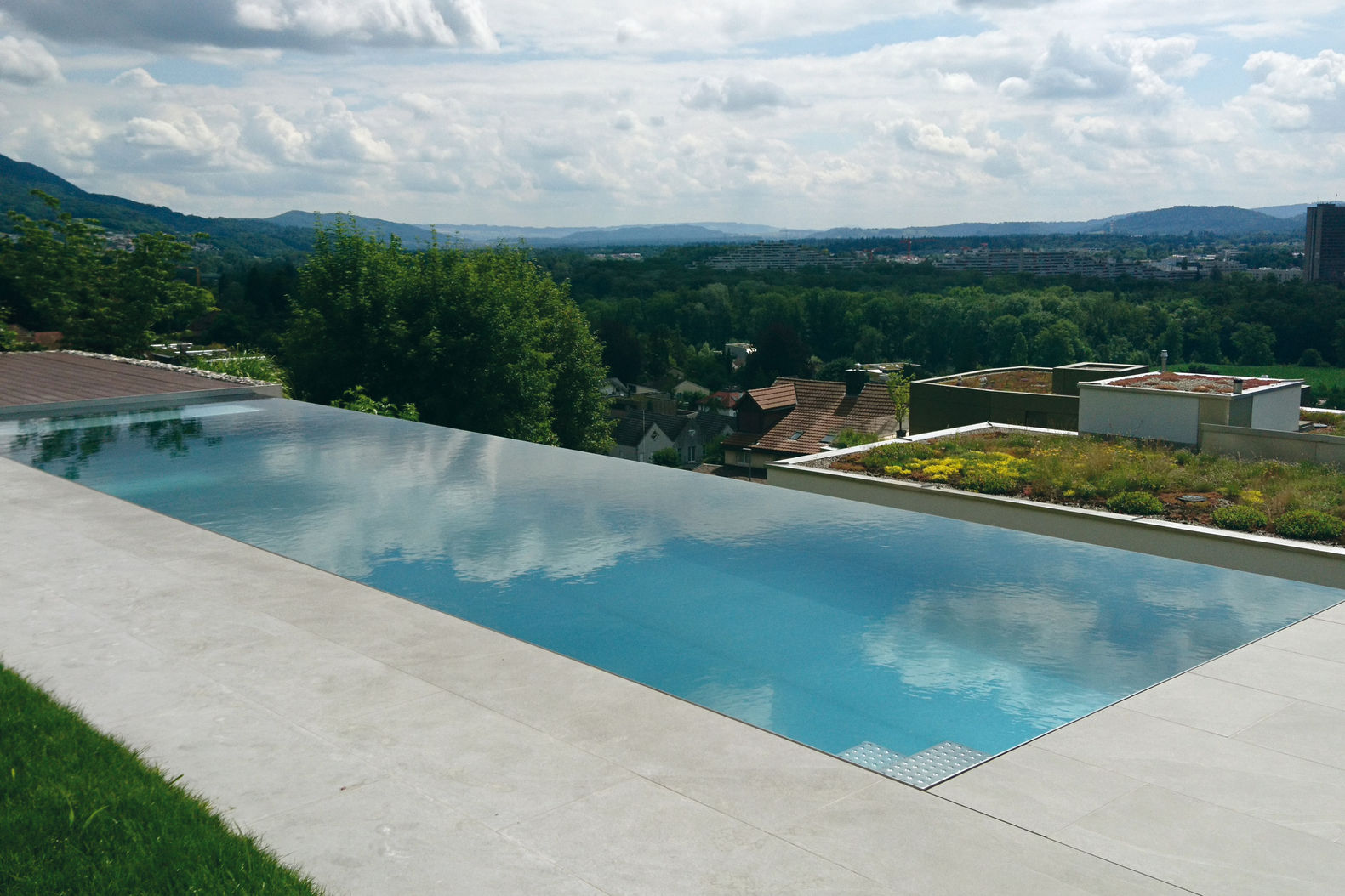 Infinitiy-Pool in Edelstahl mit freitragender Einstiegstreppe. Das zehn Meter lange Becken wurde als Fertigelement in den Garten integriert. Rolladensystem mit Rohrsitzbank und Luftsprudler, mehrere Massagedüsen. Umrandung: Feinsteinbelag und Holzterrasse. Lehnert AG.