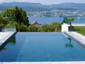 Betonpool mit Innenauskleidung in Granit, hangseitiger Überlaufrinne, automatischem Unterflurrolladen mit Solarlamellen. Filteranlage mit Salzelektrolyse. AC Schwimmbadtechnik AG.