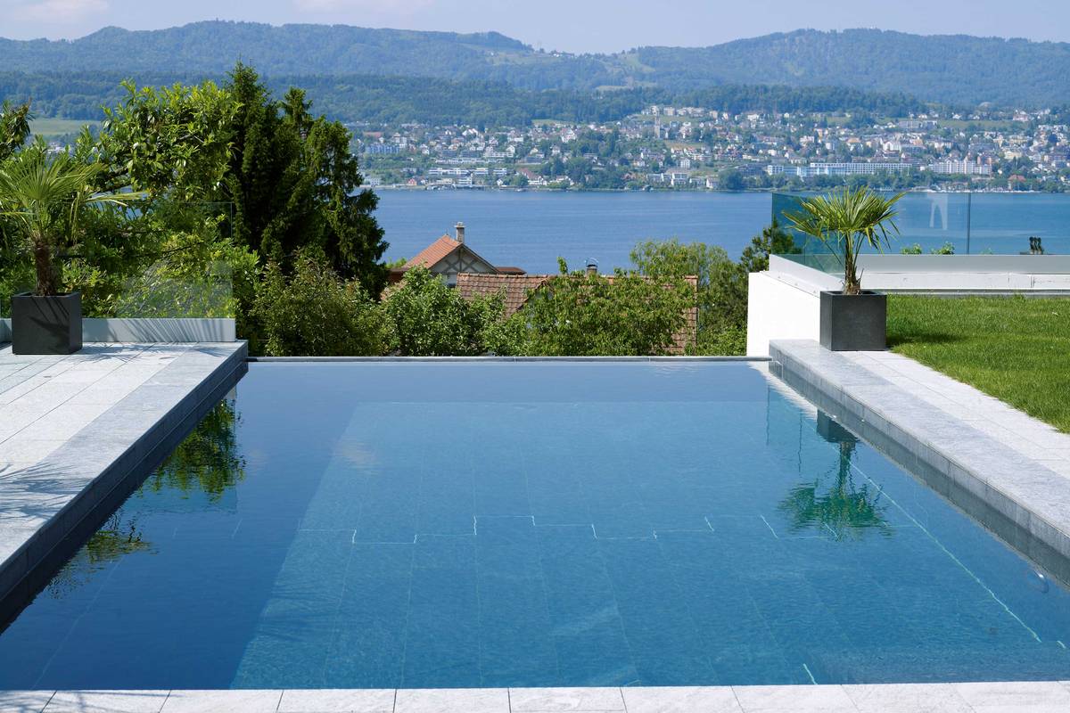 Betonpool mit Innenauskleidung in Granit, hangseitiger Überlaufrinne, automatischem Unterflurrolladen mit Solarlamellen. Filteranlage mit Salzelektrolyse. AC Schwimmbadtechnik AG.