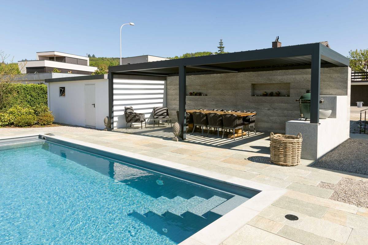 Gut kombiniert: In einen grossen Garten wurde ein acht Meter langer Pool mit Stufeneinstieg integriert. Ein Kies- und Plattenboden verbindet Pool und Wohnhaus. Zur Anlage gehört eine gedeckte Pergola mit kleiner Aussenküche, Ruhezonen und Aussendusche komplettieren den Wellnessbereich. Vivell AG Schwimmbadtechnik.