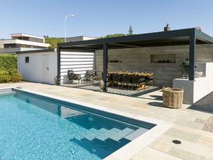 Gut kombiniert: In einen grossen Garten wurde ein acht Meter langer Pool mit Stufeneinstieg integriert. Ein Kies- und Plattenboden verbindet Pool und Wohnhaus. Zur Anlage gehört eine gedeckte Pergola mit kleiner Aussenküche, Ruhezonen und Aussendusche komplettieren den Wellnessbereich. Vivell AG Schwimmbadtechnik.