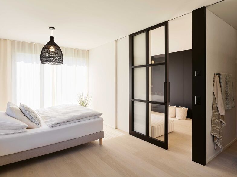 Die transparente Schiebetür ist ein Stilelement, das mehrfach verwendet wurde. Die mattschwarze Wand gibt optisch Rückhalt.