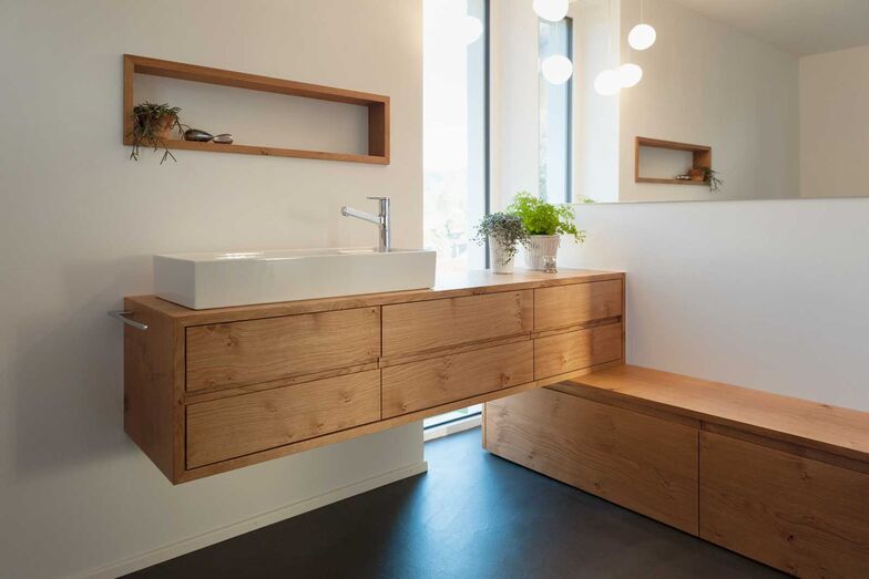 Zwei in Einem: Passend zum soliden Wachtisch in Eiche massiv mit Griffprofilen an den Schubladen wurde hier ein weiteres Möbel kombiniert, das willkommenen Stauraum bietet und gleichzeitig als Sitzbank benutzt werden kann. Die Nische über dem Waschbecken bietet Platz für Accessoires. Die grosse Spiegelwand über der Sitzbank erweitert den Raum optisch. Späti Innenausbau AG, www.spaeti.ch