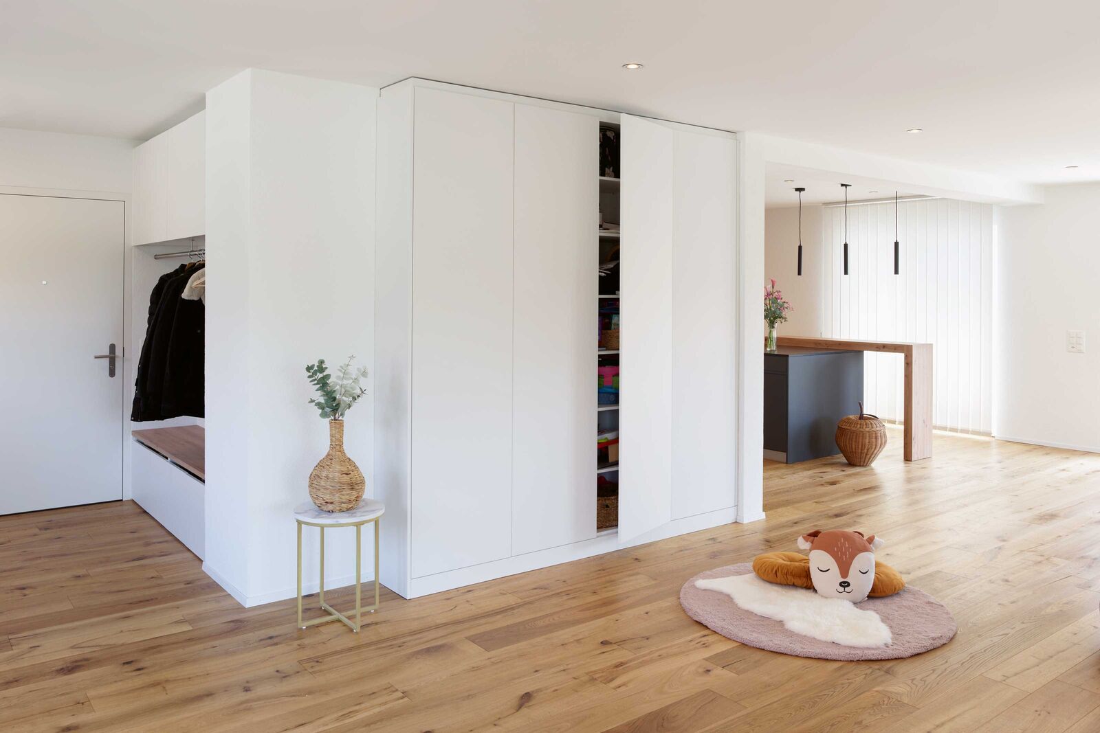 Viel Raum zum Spielen: Der grosse, offene Raum – früher ein Restaurant – wirkt schlicht, hell und aufgeräumt. Der Innenausbau wurde an die Bedürfnisse einer jungen Familie angepasst. Garderobe und Einbauschränke bieten viel Stauraum, dank Tip-On-Mechanismus sind keine Griffe nötig. Der hölzerne Sitz passt zum Holzboden. Um die grosse Kochinsel, das Zentrum des Raums, wird regelmässig «Fangis» gespielt. Vorratsschrank, Kühlschrank, Backofen/Steamer, Backofen/Mikrowelle sowie die Kaffeenische sind in einer weissen Hochschrankfront in der Küche untergebracht. Loosli AG, www.loosli.swiss