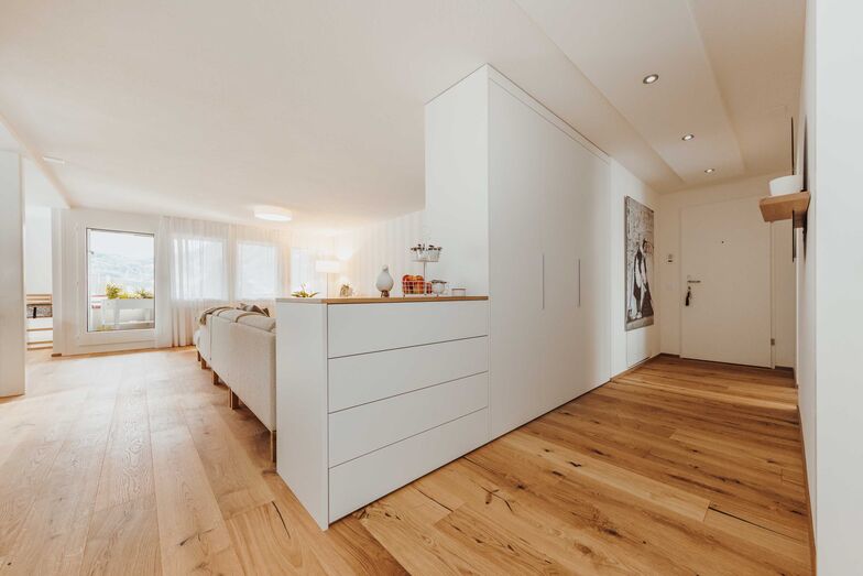 Stauraum und Raumtrenner Um keinen Platz zu verschenken und möglichst viel Wohn- und Stauraum zu haben, ist der Garderobenschrank gleichzeitig Raumtrenner und schirmt das Wohnzimmer vom Gang ab. Die über die Rückseite des Schranks gezogene helle Wohnzimmertapete kaschiert das Möbel elegant. In der Verlängerung des Schranks schliesst sich eine Kommode an. Deren Abdeckung in Eiche furniert bildet den dekorative Abschluss des Elements und passt gut zum Eichenparkett. Alpnach Schränke AG, www.alpnachnorm.ch