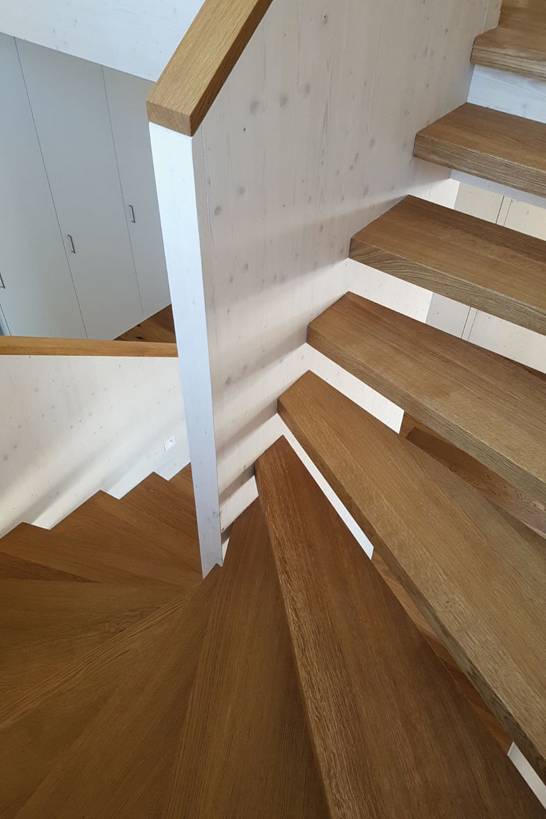 Die halb gewundene Treppe ist mit verdeckter Konstruktion an den Holzwänden befestigt. Tritte und Brüstungsabdeckung in Eiche, gebürstet und geölt, wurden an die Farbe des Parketts angepasst. Ambauen Treppen AG.