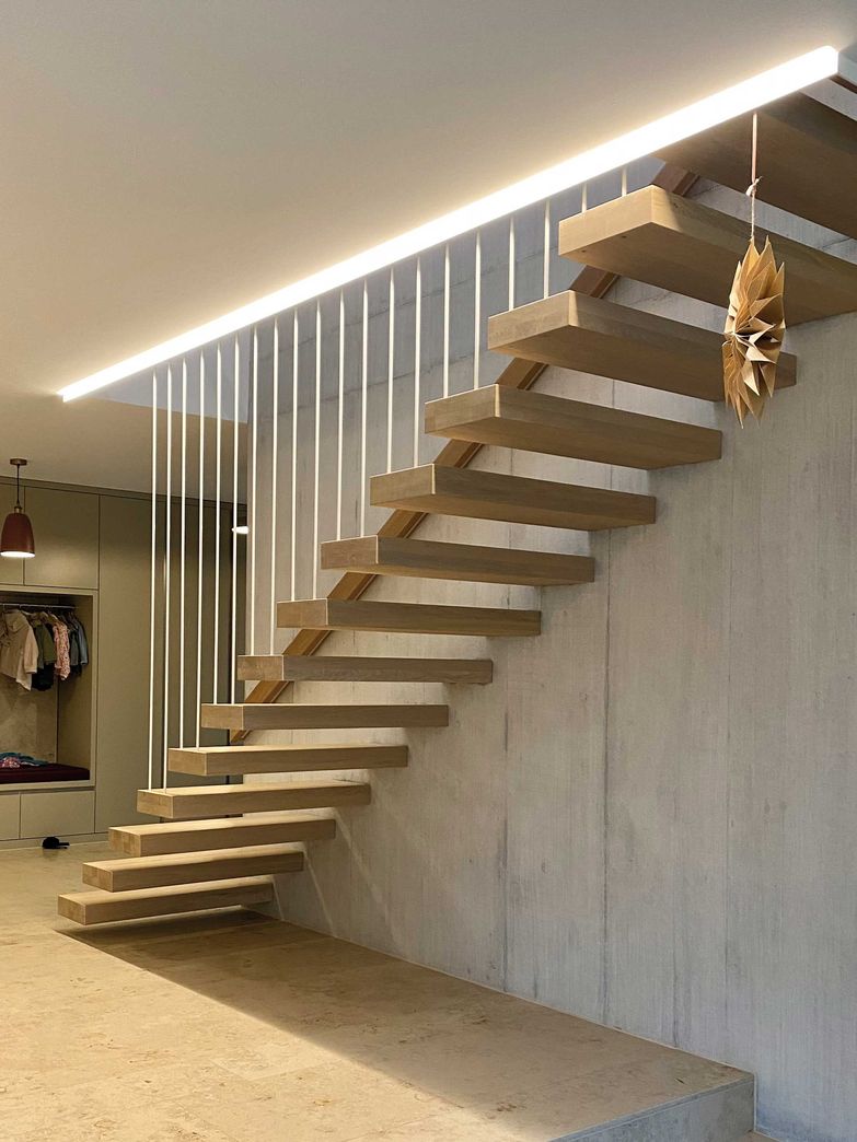 Freitragende Eichenstufen mit Geländer aus einbrennlackierten Stahlsprossen vor Sichtbeton. Die LED-Beleuchtung im Deckenblech rückt die Komposition ins rechte Licht. Langegg Treppenbau.