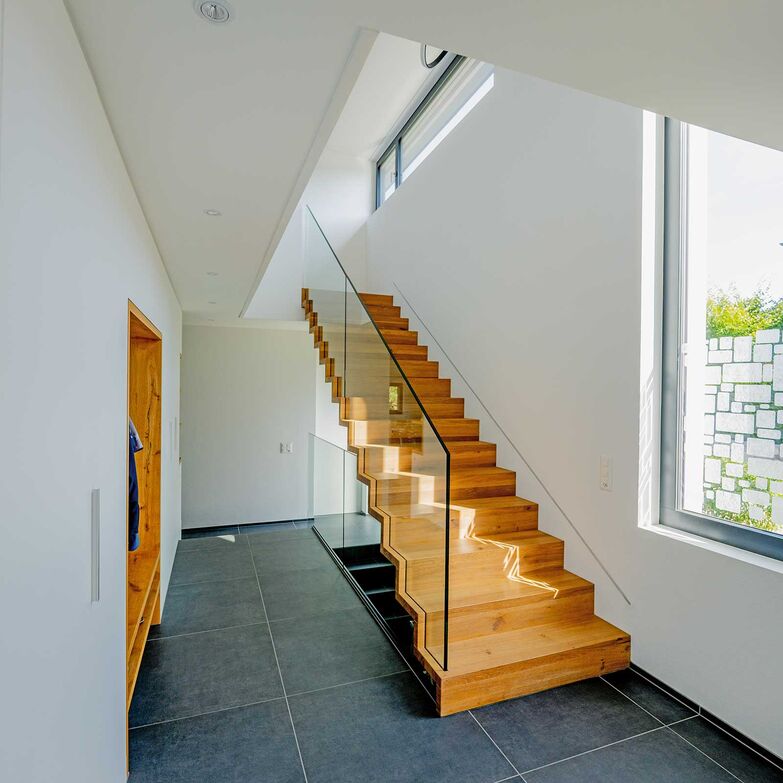 Die Verbindung von Massivholz mit dem rahmenlosen Glasgeländer unterstreicht das minimalistische Design und die Leichtigkeit dieser Faltwerktreppe. Keller Treppenbau AG, www.keller-treppen.ch