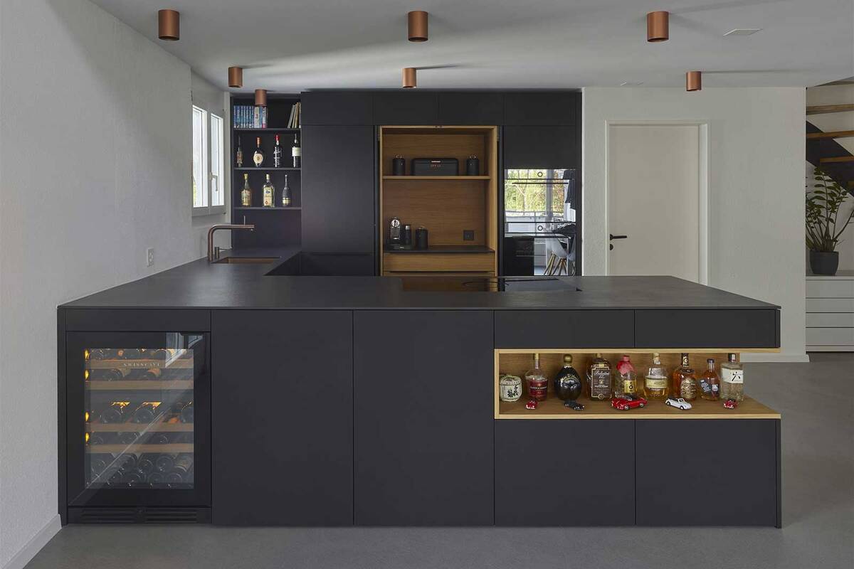 Bei diesem Küchenumbau wurden mattschwarze Fronten mit einer grosszügigen Nische in Eiche massgefertigt. Die LED-Beleuchtung und die mattschwarzen Griffprofile aus Aluminium erzeugen eine visuell ansprechende Komposition. Oesch Innenausbau AG.