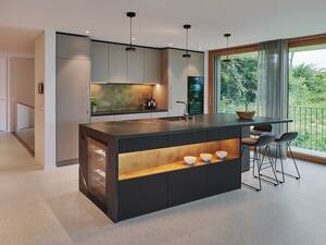 Ein Bijou mit Ecken und Kanten: Die schwarze Kochinsel harmoniert mit den Hochschränken im eleganten Naturgrau. Messing-Rückwände und die lederne Oberflächenstruktur des Negresco-Granits runden die edle Küche ab. Brunner Küchen.