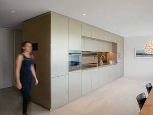 Die champagnerfarbene Einzeiler-Küche zeigt, wie leicht und elegant eine Raumtrenner-Küche wirken kann. Der bronzefarbene Küchenspiegel öffnet den Raum. Für ein stimmiges Bild sorgt auch die Lavastein-Abdeckung. Elbau.