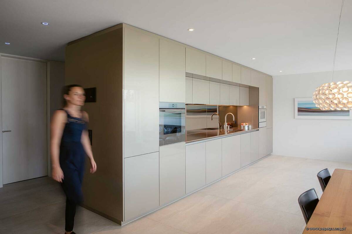 Die champagnerfarbene Einzeiler-Küche zeigt, wie leicht und elegant eine Raumtrenner-Küche wirken kann. Der bronzefarbene Küchenspiegel öffnet den Raum. Für ein stimmiges Bild sorgt auch die Lavastein-Abdeckung. Elbau.