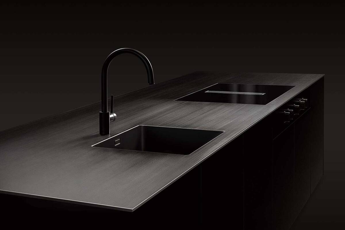 Basis der Küchenabdeckung «Vulcano» ist eine warmgewalzte Platte aus Edelstahl, welche mit einer keramischen Beschichtung geschwärzt wird. In die pflegeleichte und korrosionsbeständige Oberfläche lässt sich das Spülbecken fugenlos einschweissen. Morath Design.