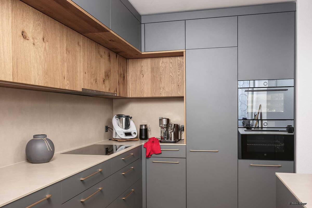 «Trendino» punktet mit viel Stauraum und hoher Alltagstauglichkeit. Graphitfarbene Flächen, die zurückversetzten Schrankfronten in Eiche und die goldenen Griffe bilden ein optisch spannendes Ensemble. Veriset.