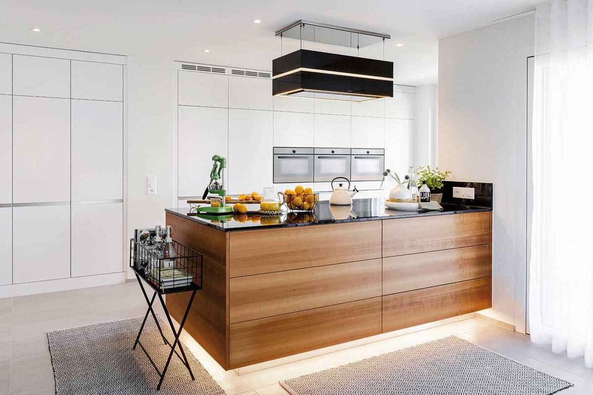 Die Sockelbeleuchtung lässt die Kücheninsel mit charakteristischer Maserung schwebend wirken. Hochwertige Materialien und präzise Verarbeitung machen die Qualität bei dieser Küche mit Geräten auf ergonomischer Höhe sichtbar. Herzog Küchen.