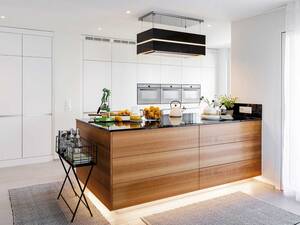 Die Sockelbeleuchtung lässt die Kücheninsel mit charakteristischer Maserung schwebend wirken. Hochwertige Materialien und präzise Verarbeitung machen die Qualität bei dieser Küche mit Geräten auf ergonomischer Höhe sichtbar. Herzog Küchen.