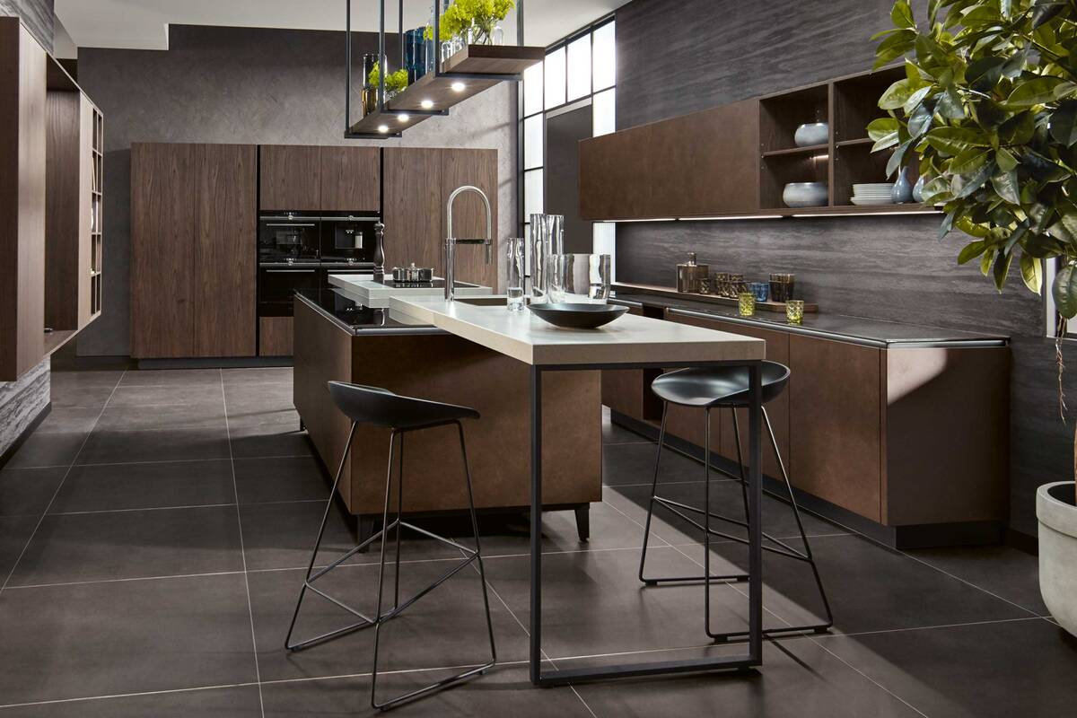 Die Insel wird von zwei Thekenflügeln aus Keramik eingerahmt. So sind die Wege zwischen Spülen und Kochen kurz. «Y-line» in «Terrazzo goldbraun» und «Sherwood dunkelbraun». Hans Eisenring AG.