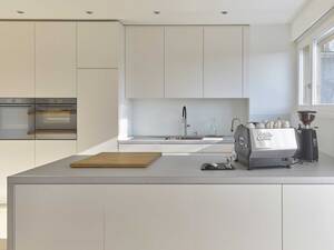 Die helle Küche besticht durch ihre Abdeckungen und Seiten aus Echtbeton. Die Fronten sind spritzlackiert. Das Wandboard schenkt zusätzlichen Platz für Küchenutensilien. Oesch Innenausbau AG.