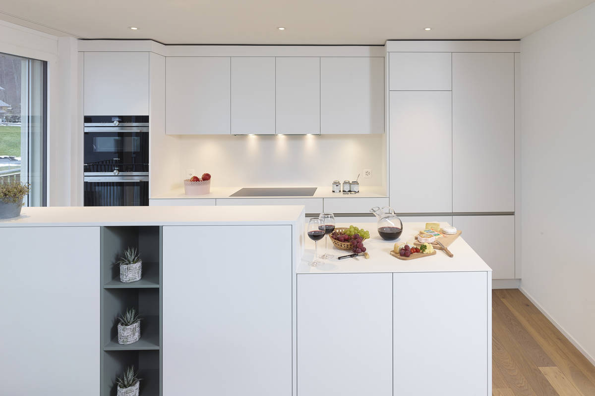 Grifflose Fronten, hier in Weiss «Porzellan», geben der weissen Küche noch mehr Eleganz. Die LED-Beleuchtung sorgt fürs richtige Licht. Alpnach Norm.
