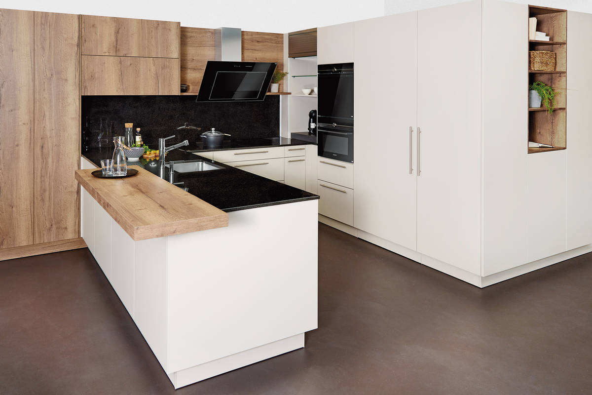 Die Schwarz-Weiss Kombi der Küche wird durch die edlen Holzoptik-Elemente gebrochen. Die intelligente Abzugshaube sorgt für das technische Highlight. Sabag.