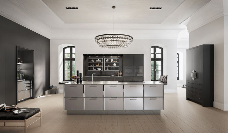 Mit der symmetrischen Anordnung, starken Schwarz-Weiss-Kontrasten und Fronten mit facettierten Rahmen interpretiert die Stilwelt «Classic» klassische Themen neu. Feine Arbeitsplatten und Seitenwangen in Edelstahl fassen die Insel ein.